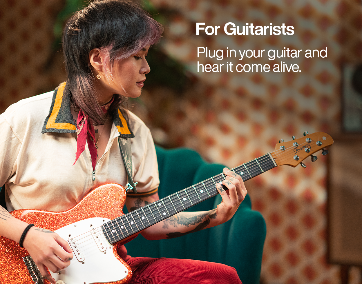 Guitarist playing an orange sparkle electric guitar at home, with text reading 'For Guitarists: Plug in your guitar and hear it come alive'.